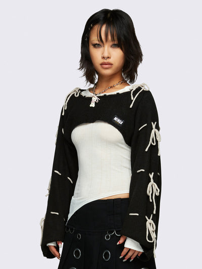 Black knitted shrug with white tie bows, designed in a bolero style with long, wide sleeves.
