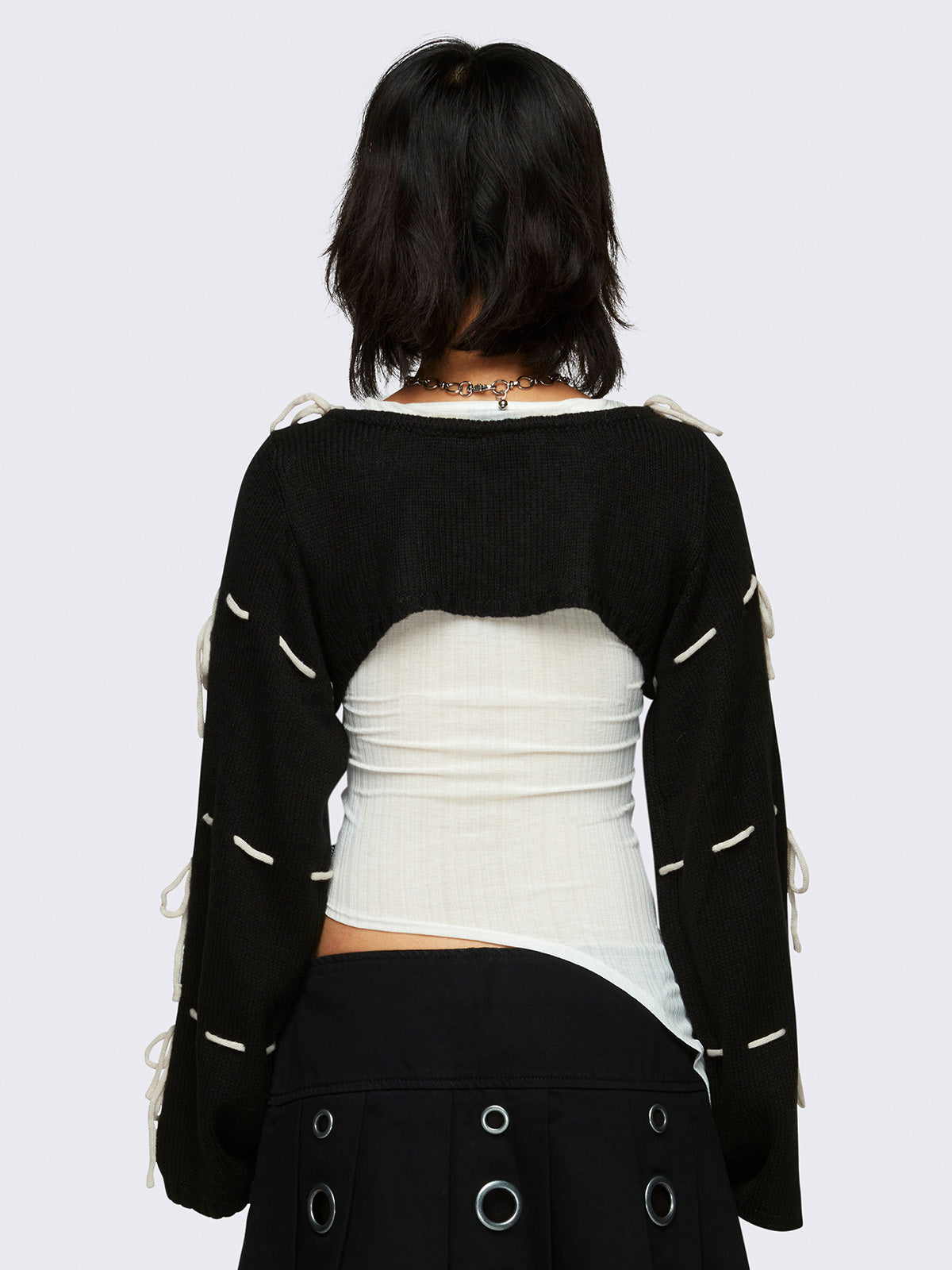 black knitted shrug with white tie bows, designed in a bolero style with long, wide sleeves.
