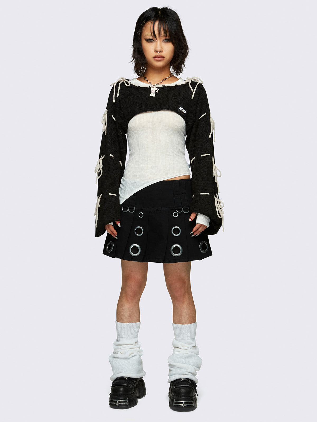 Black knitted shrug with white tie bows, designed in a bolero style with long, wide sleeves.