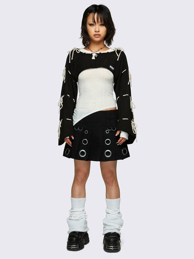 Black knitted shrug with white tie bows, designed in a bolero style with long, wide sleeves.