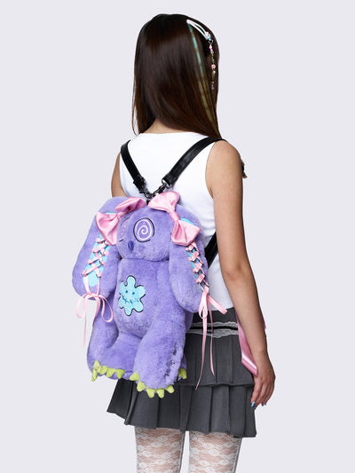 Purple furry bunny plush backpack with pink lace-up ribbons and bows on the bunny ears, embroidered details, and a back zipper pocket.