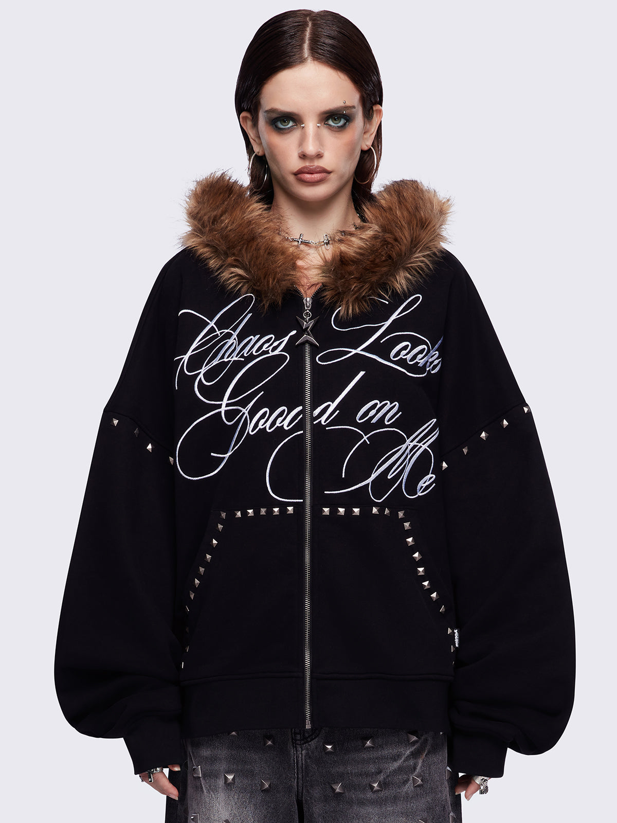 Black zip up hoodie jacket featuring a brown faux fur hood, "Chaos looks good on me" graphic embroidery and stud details.