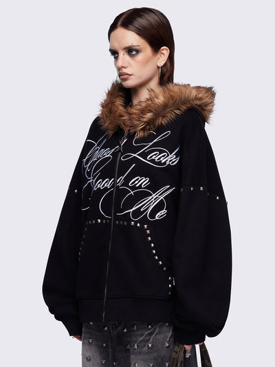 Black zip up hoodie jacket featuring a brown faux fur hood, "Chaos looks good on me" graphic embroidery and stud details.