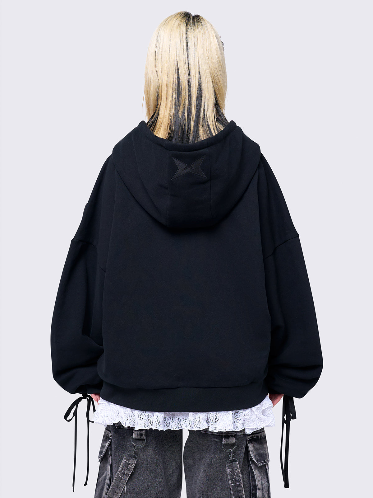 Black zip-up hoodie with lace corset details along the sleeves and front. Features a drawstring hood, zip fastening, long sleeves, and an oversized fit.