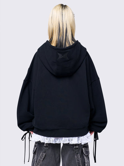 Black zip-up hoodie with lace corset details along the sleeves and front. Features a drawstring hood, zip fastening, long sleeves, and an oversized fit.
