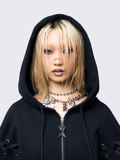 Black zip-up hoodie with lace corset details along the sleeves and front. Features a drawstring hood, zip fastening, long sleeves, and an oversized fit.