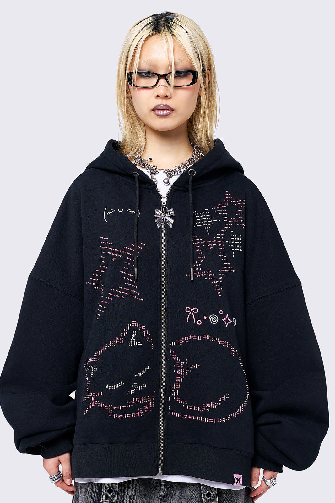 Black zip-up hoodie jacket featuring a pink cat and stars graphic with stud and embroidery details. Designed with a drawstring hood, zip fastening, long sleeves, ribbed trims, and an oversized fit.