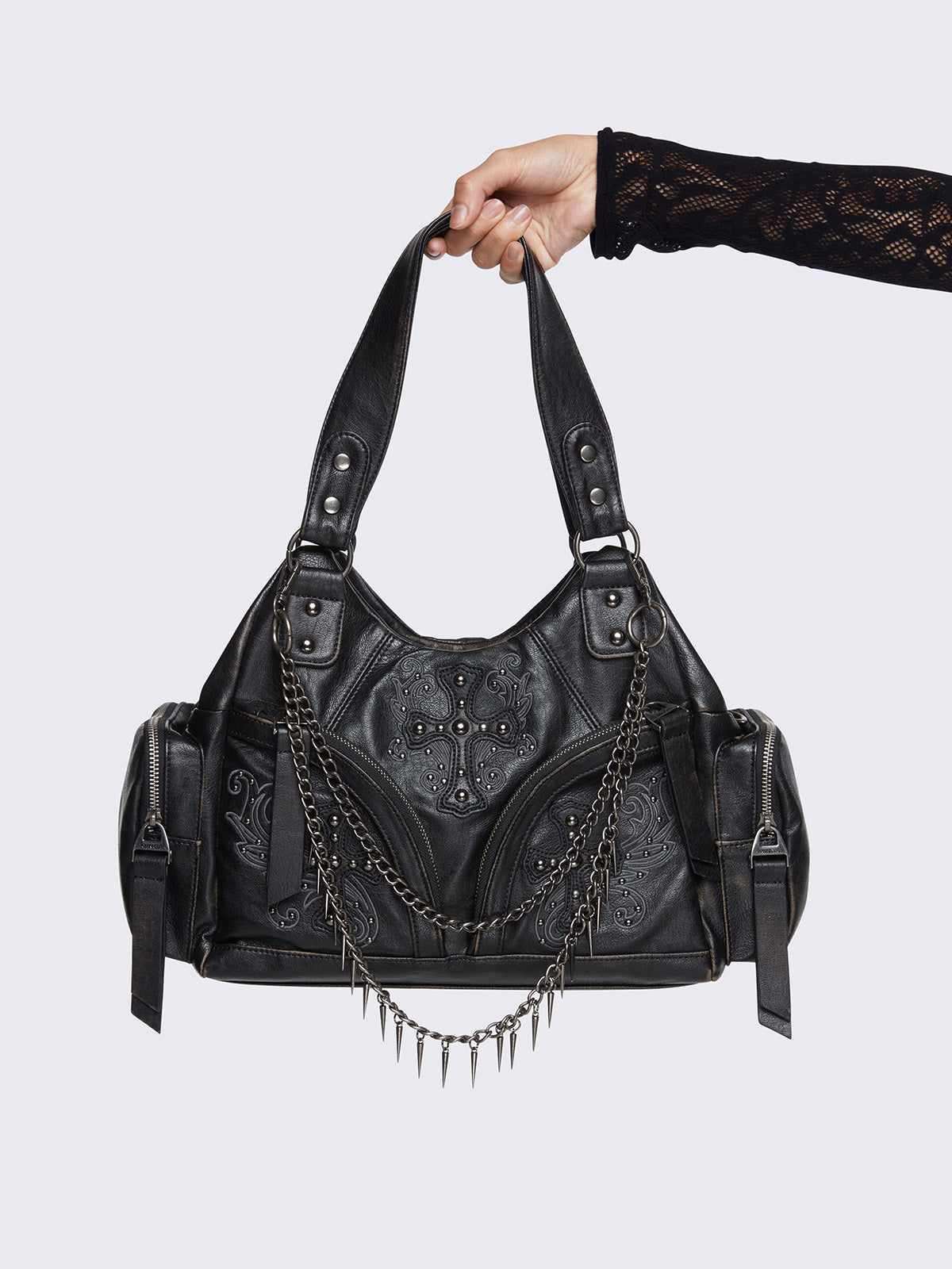 Black faux leather shoulder bag with silver chains, spike charms, side pockets, and embroidered cross detail on the front.