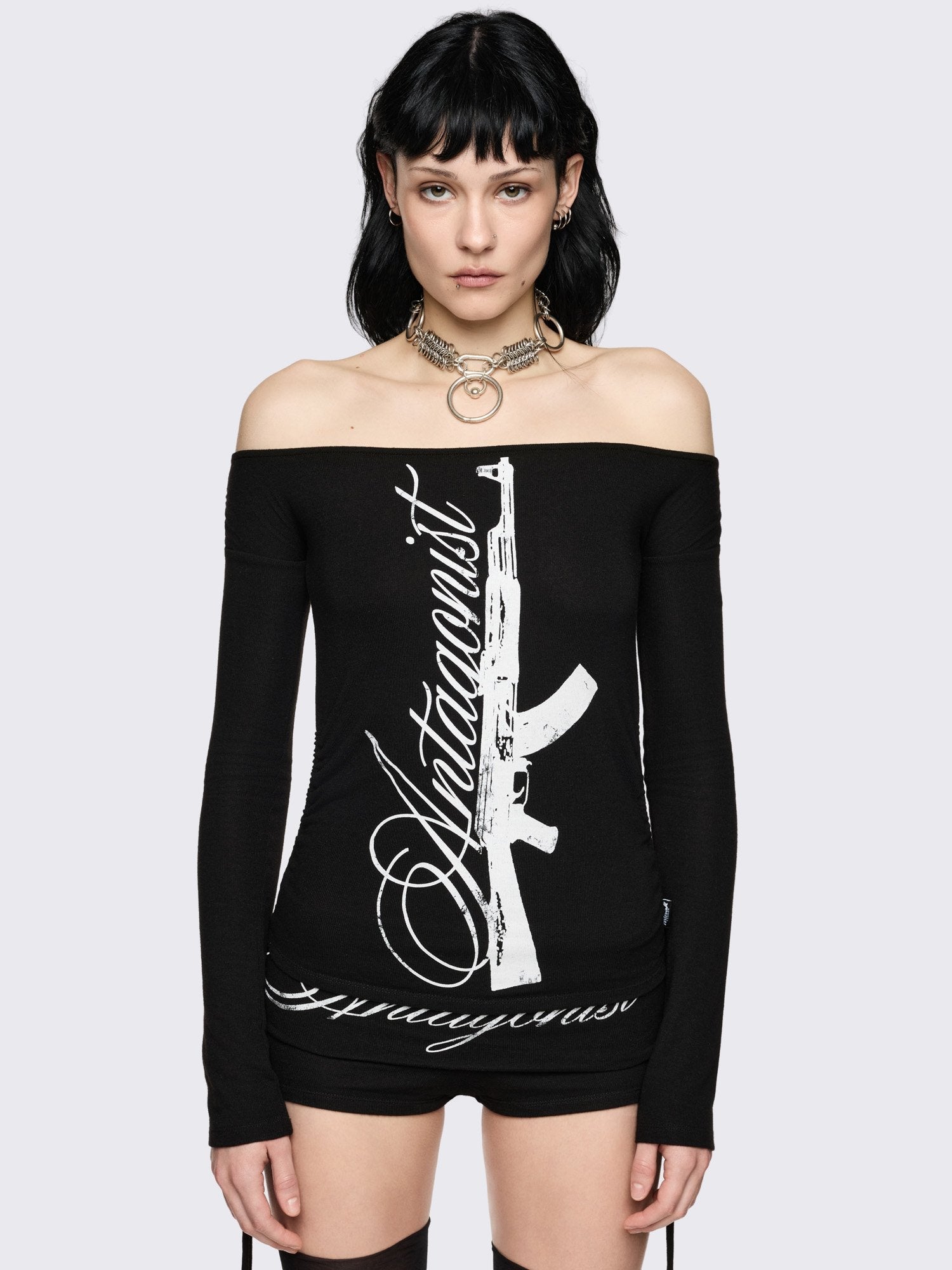Black long sleeve off-shoulder top with "Antagonist" gun graphic front print and ruched tie side