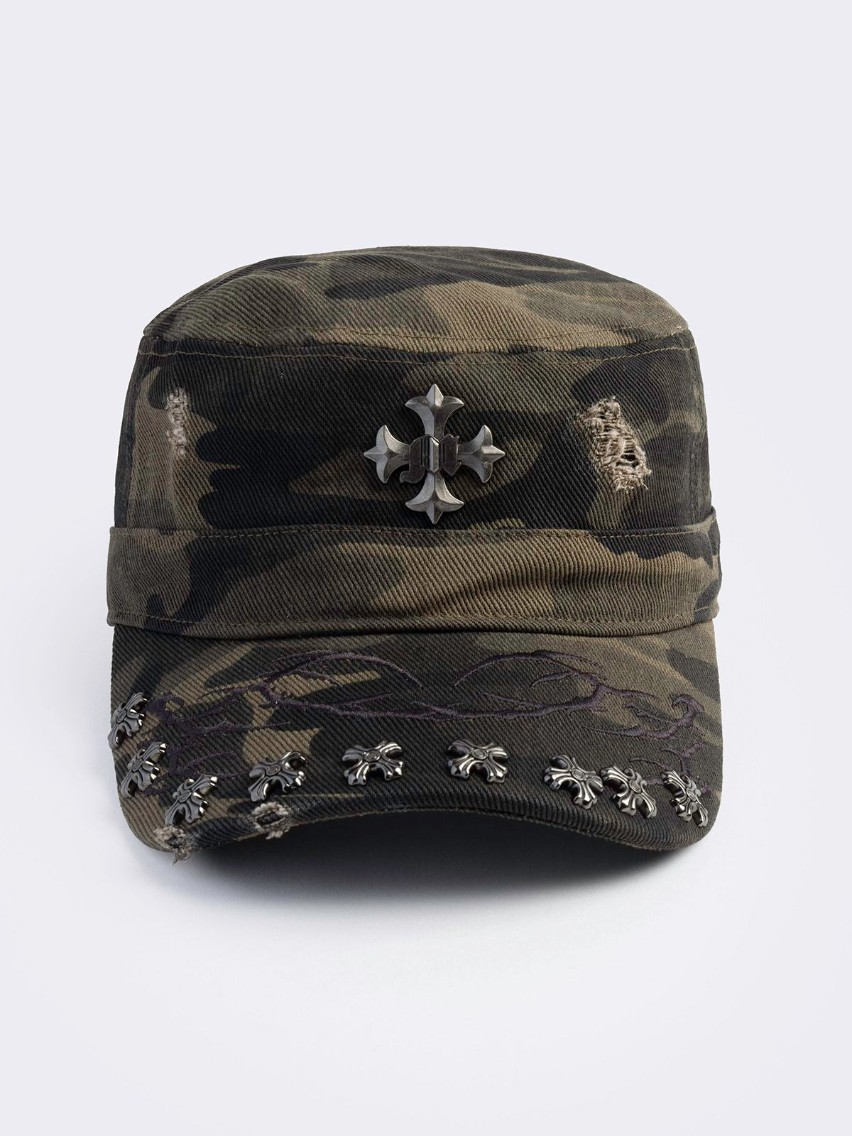 flat-top military cadet cap in a green and brown forest camouflage print, featuring a large silver gothic cross emblem on the front and heavy distressed rips.