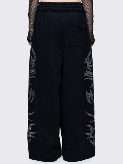 Loose-fit wide-leg sweatpants featuring a large, detailed tribal sigil pattern made of silver rhinestones running down the side seam.