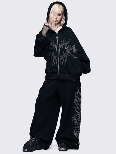 Loose-fit wide-leg sweatpants featuring a large, detailed tribal sigil pattern made of silver rhinestones running down the side seam.