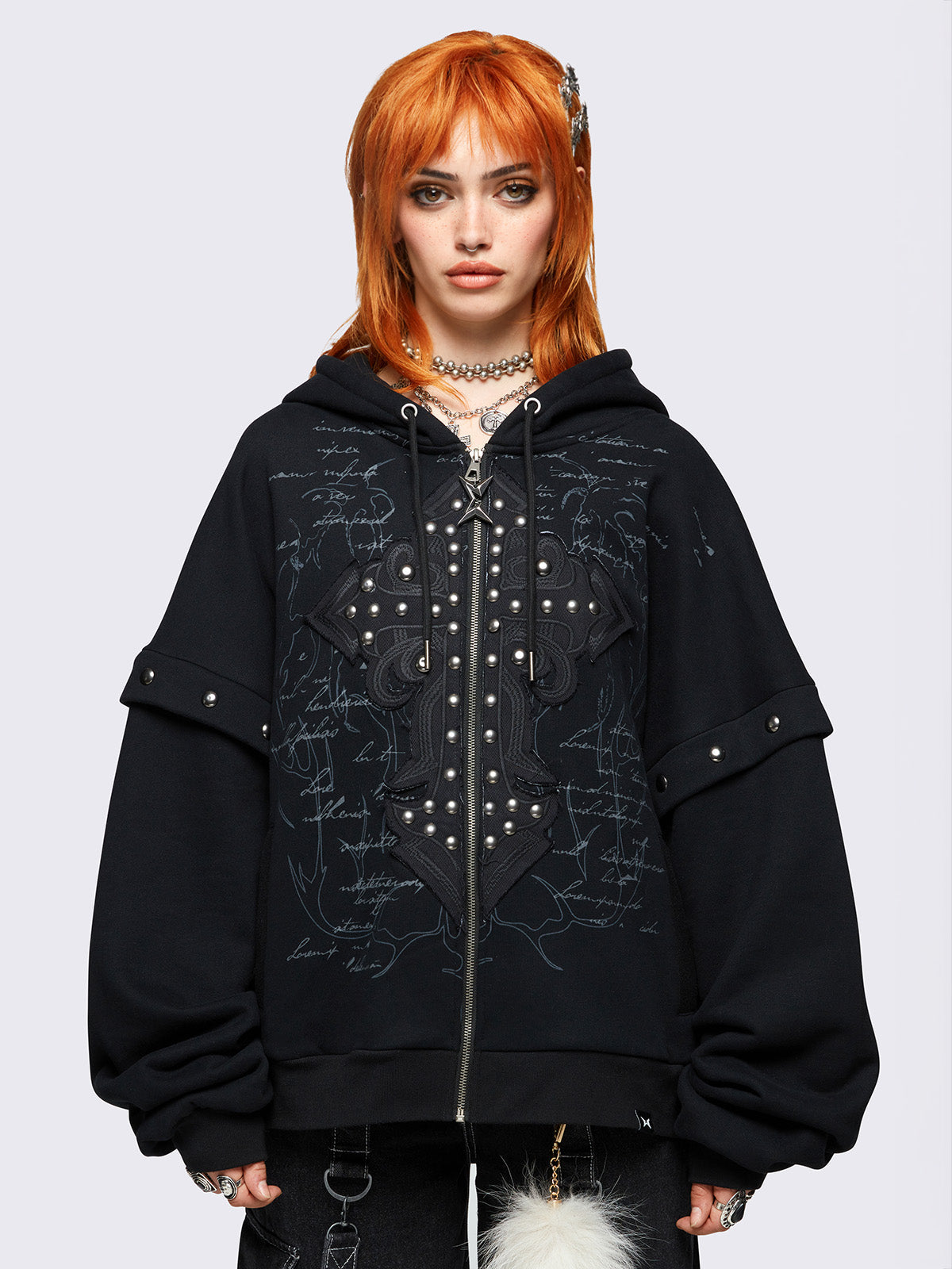 Black layered zip-up hoodie featuring gothic lettering and a cross patch with studded accents, oversized fit, drawstring hood, and zip fastening.