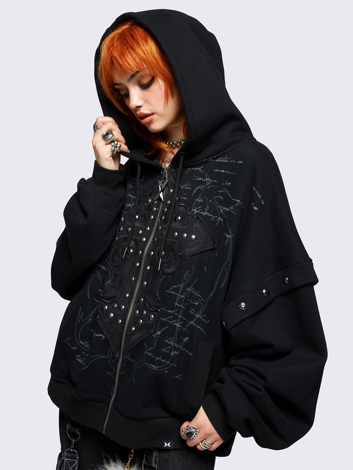 Black layered zip-up hoodie featuring gothic lettering and a cross patch with studded accents, oversized fit, drawstring hood, and zip fastening.