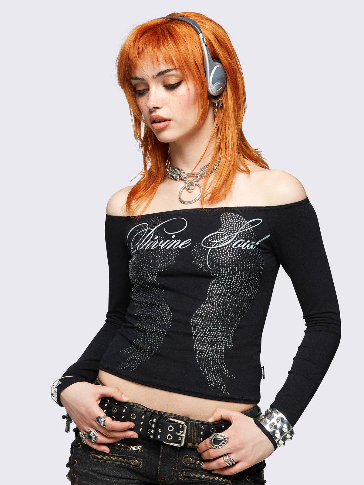 Black long sleeve off-shoulder top featuring hot fix stud wings and "Divine soul" graphic print.