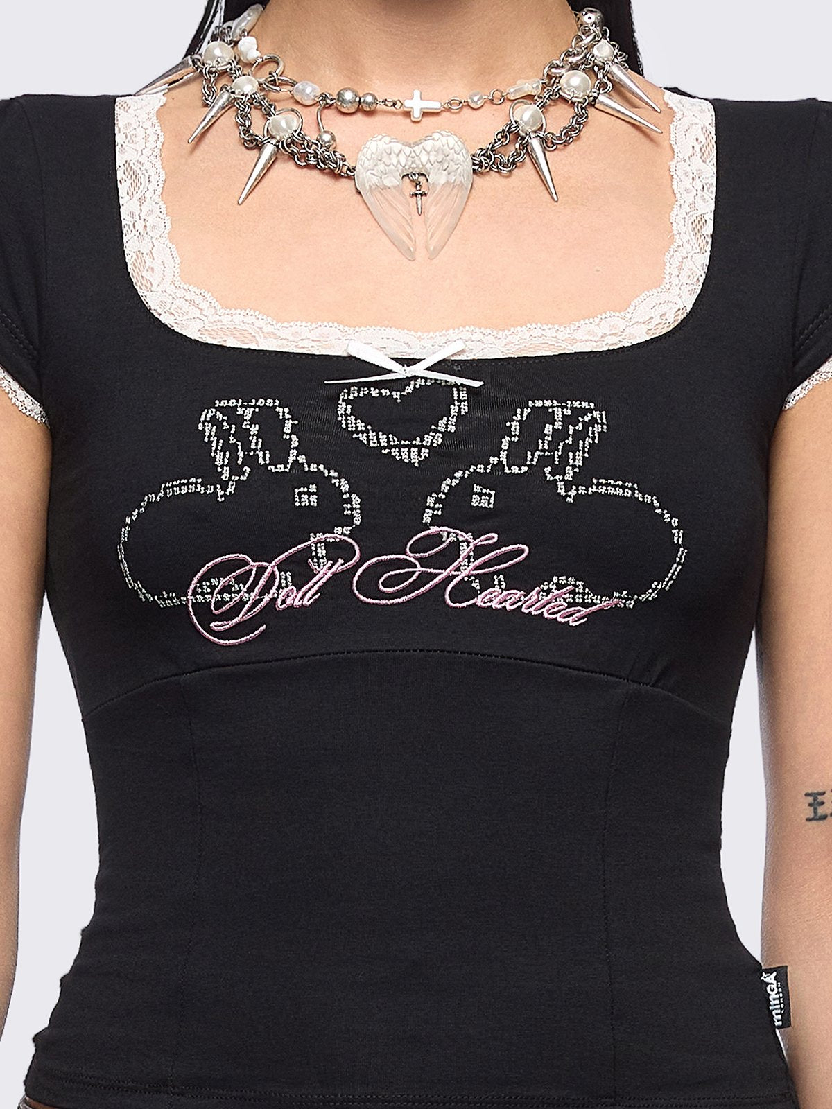 Black baby tee with "Doll Hearted" and bunnies graphic embroidery, white lace at seams and bow details.
