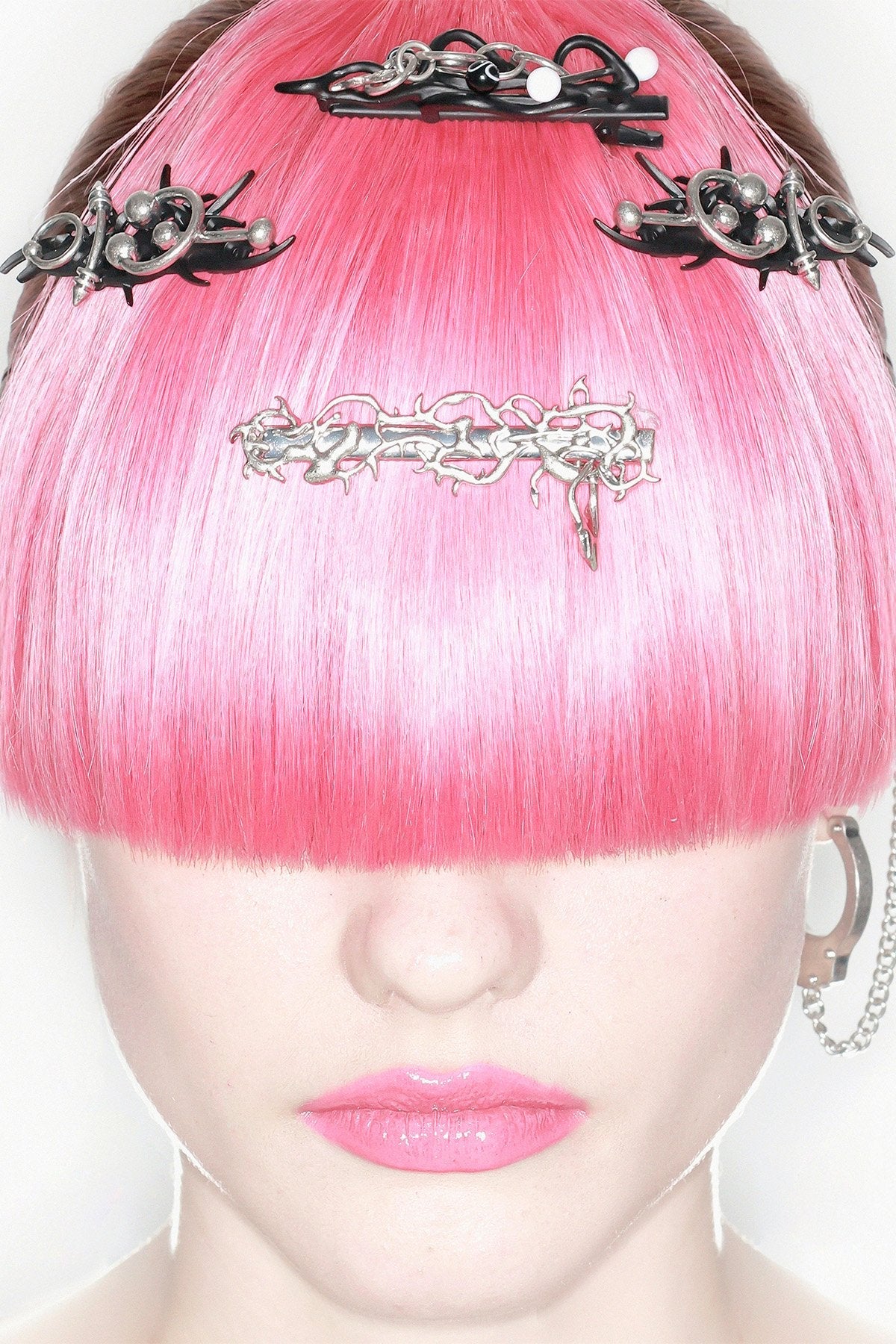 Black and silver metal hair clips with piercing, chains and sigilism details in a goth cyber style.