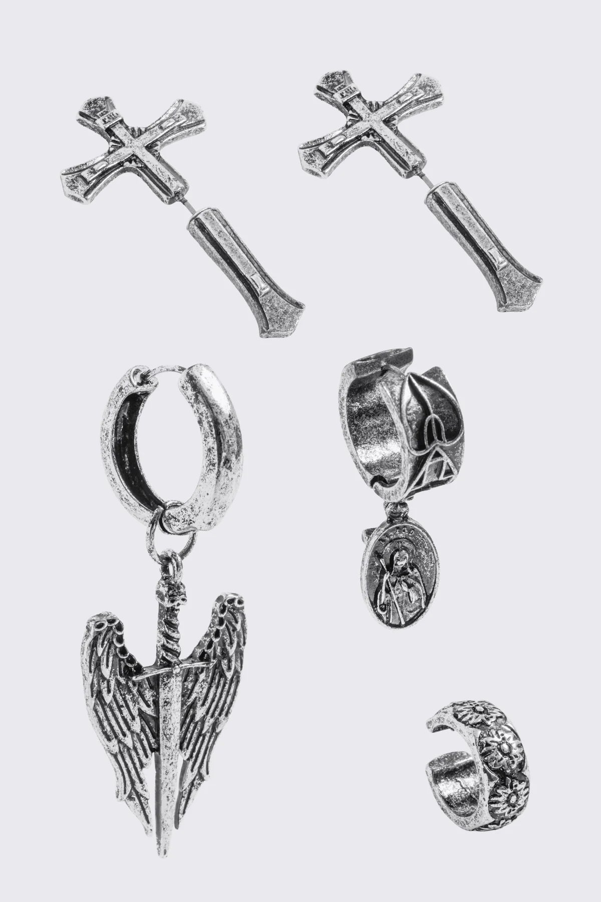 A 5-piece set of mismatched silver-toned earrings and an ear cuff featuring gothic and religious motifs, including crosses, a Virgin Mary medallion, and a winged sword dangle.