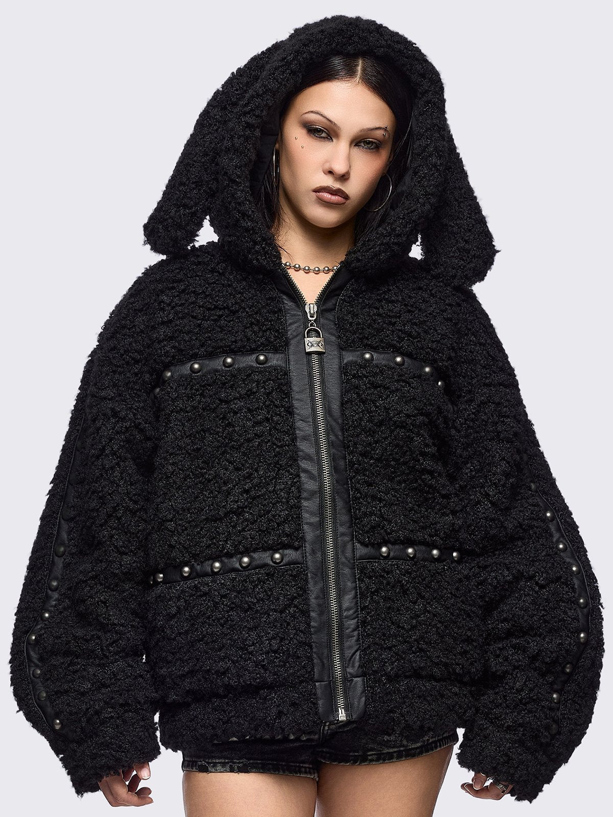Black faux fur coat featuring a bunny ear hood and faux leather details with silver studs.