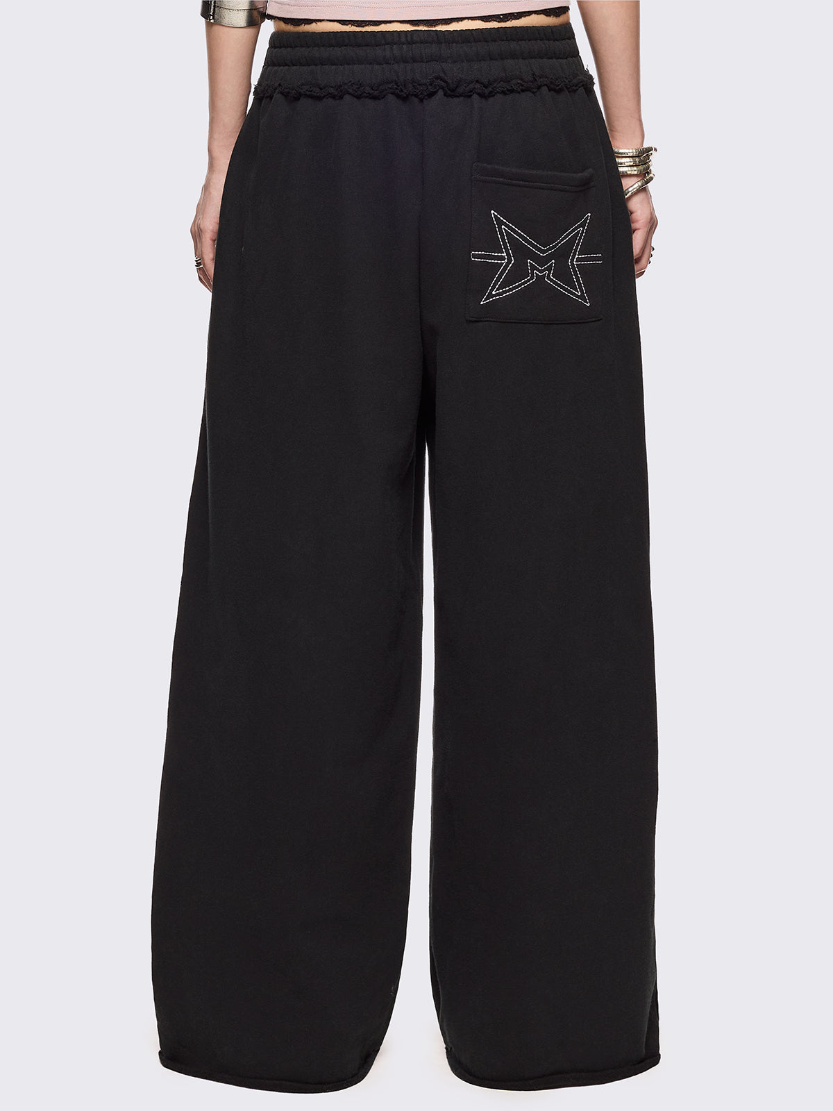 Black oversized sweatpants with all-over white emoticon and heart graphics in a playful ASCII/kaomoji style, styled in a relaxed streetwear fit.