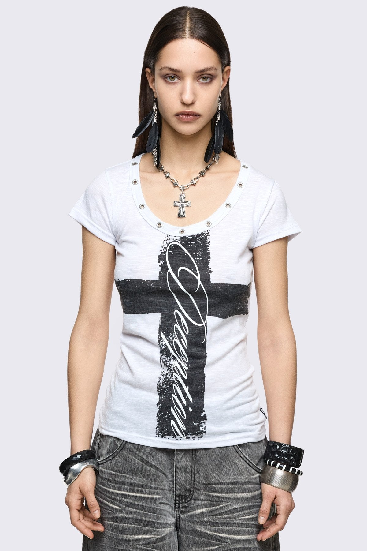 White baby tee in stretch jersey with black cross graphic, scoop neck eyelet details, and grunge vibe.