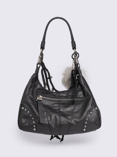 A black leather hobo bag decorated with silver studs, metallic charms, braided leather, and a large grey and white fur tail charm.