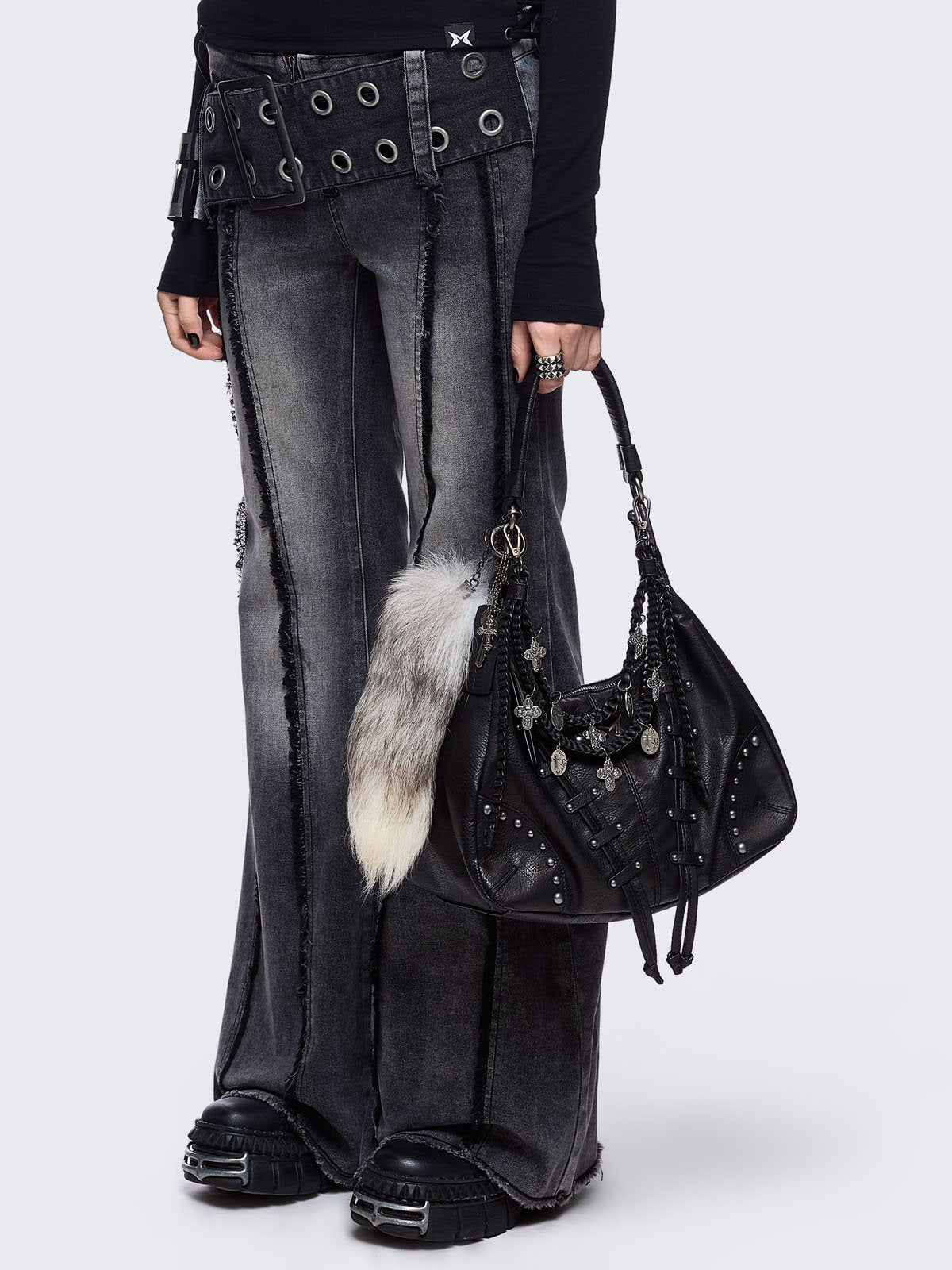 A black leather hobo bag decorated with silver studs, metallic charms, braided leather, and a large grey and white fur tail charm.