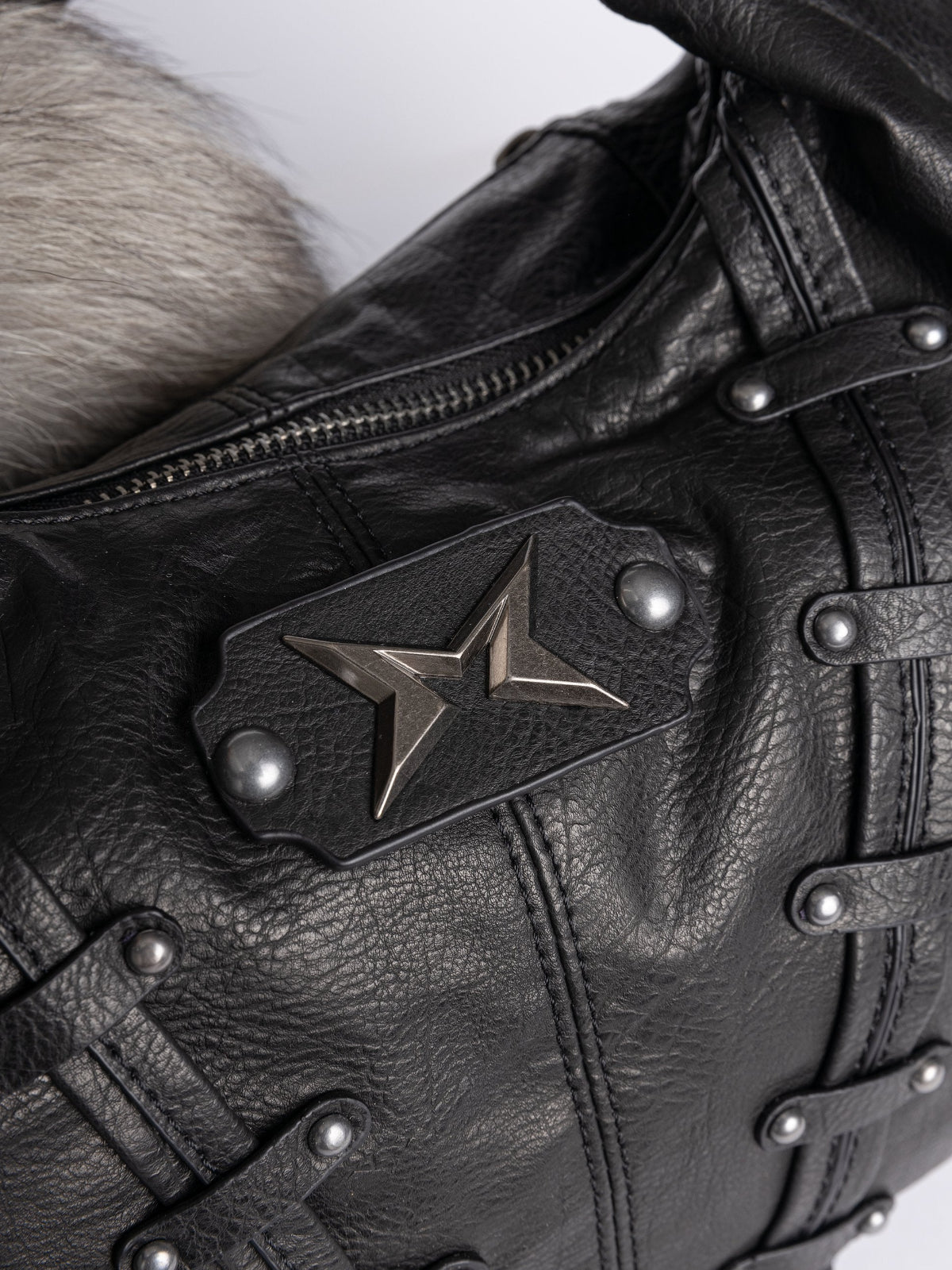 A black leather hobo bag decorated with silver studs, metallic charms, braided leather, and a large grey and white fur tail charm.