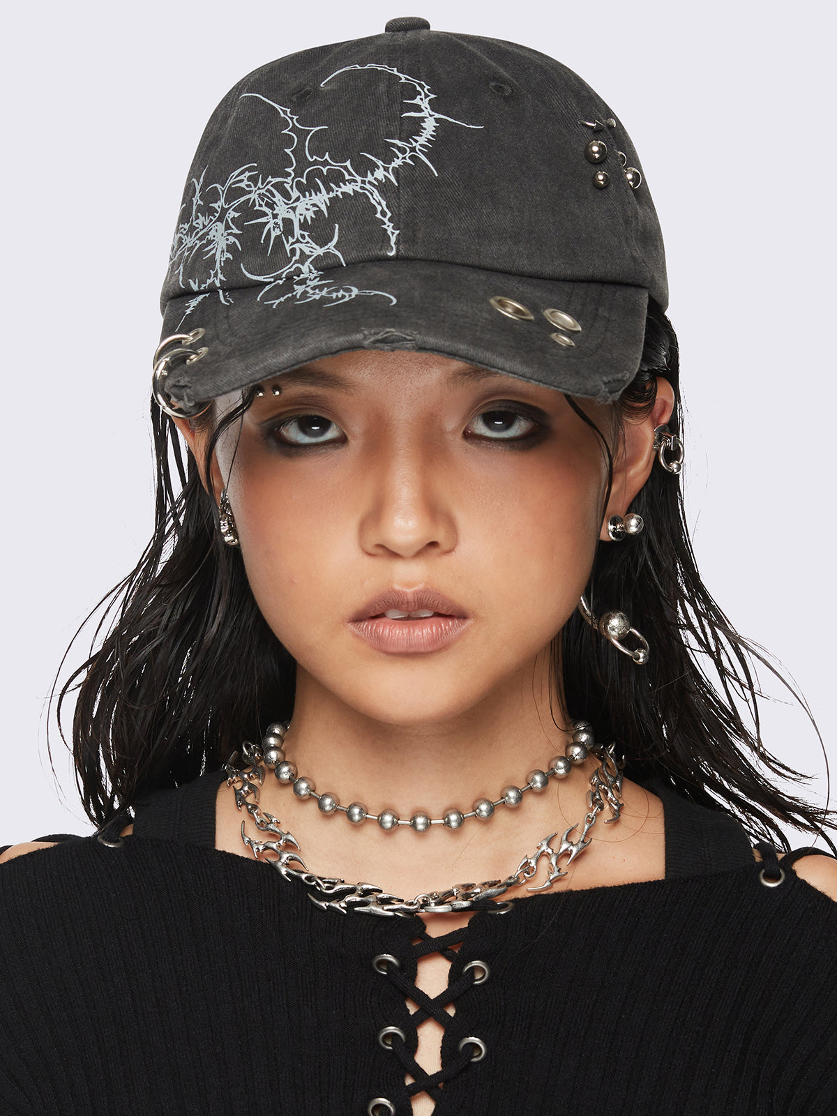 Black washed baseball cap with sigilism graphic print and distressed, eyelet and piercing details.