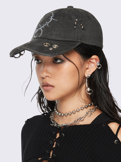 Black washed baseball cap with sigilism graphic print and distressed, eyelet and piercing details.