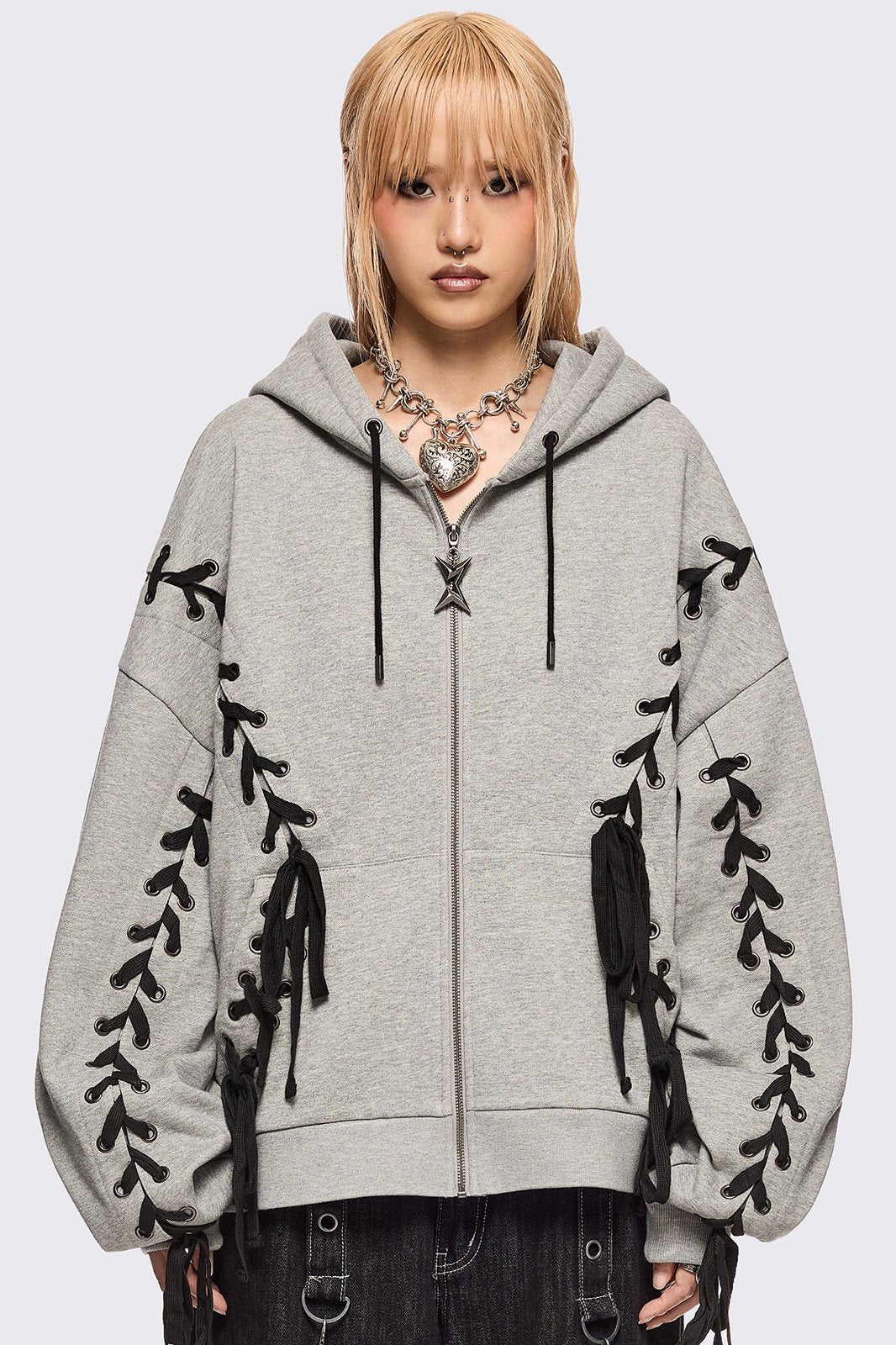 Grey marl zip-up hoodie with black lace corset details along the sleeves and front. Features a drawstring hood, zip fastening, long sleeves, and an oversized fit.