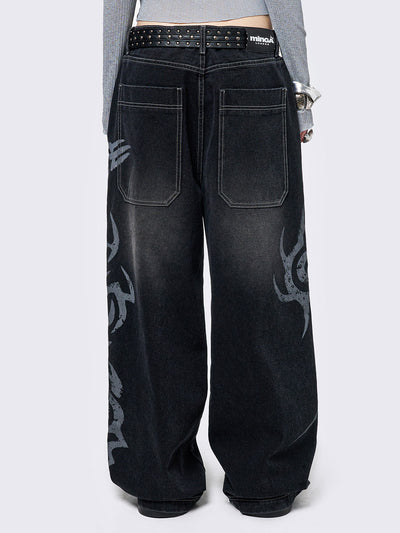 Black washed baggy jeans with a gritty grey sigilism side print, edgy white contrast stitching, regular waist, wide leg, and a relaxed, oversized fit for a grunge-inspired look.
