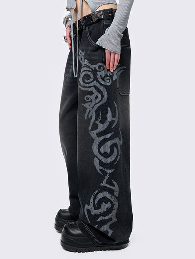 Black washed baggy jeans with a gritty grey sigilism side print, edgy white contrast stitching, regular waist, wide leg, and a relaxed, oversized fit for a grunge-inspired look.