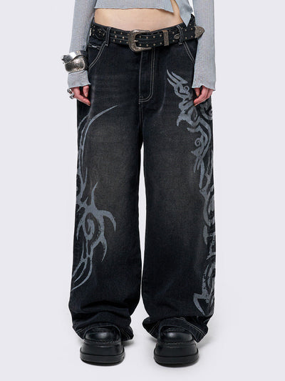 Black washed baggy jeans with a gritty grey sigilism side print, edgy white contrast stitching, regular waist, wide leg, and a relaxed, oversized fit for a grunge-inspired look.