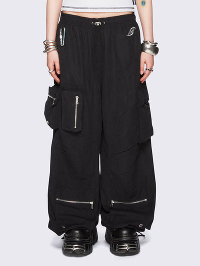 Black tech cargo parachute pants featuring multiple utility pockets with zipper and carabiner hardware detail - edgy, utility-inspired streetwear style.