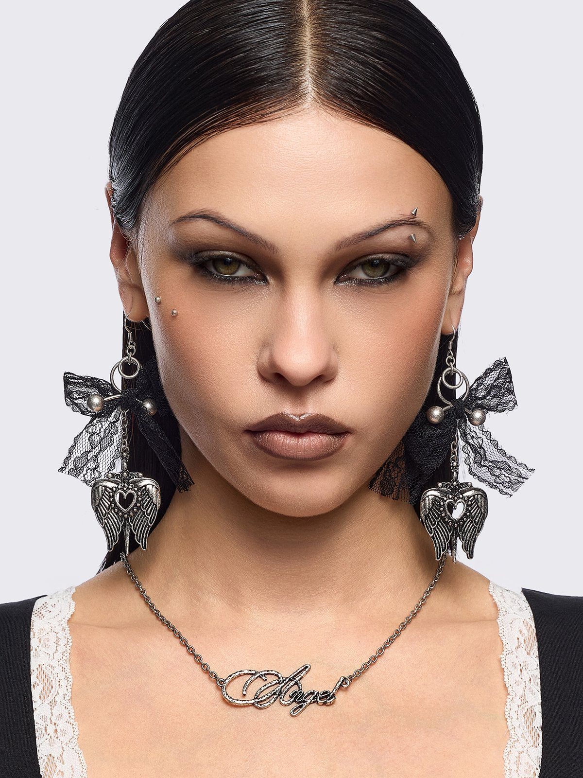 Silver dangle earrings with winged heart pendant and back lace bows and piercing details.