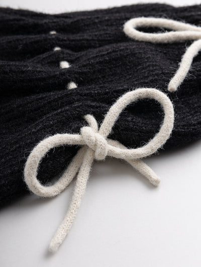 Black knitted leg warmers with white tie bows and a flared style.