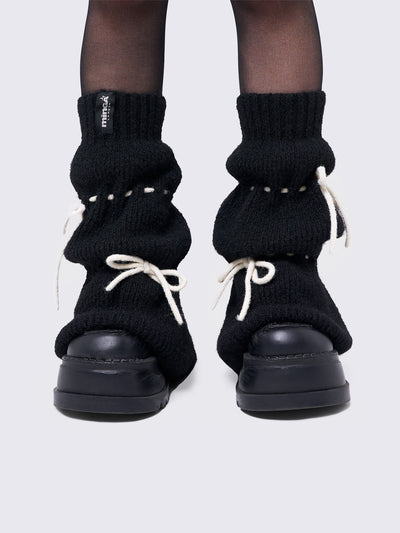 Black knitted leg warmers with white tie bows and a flared style.