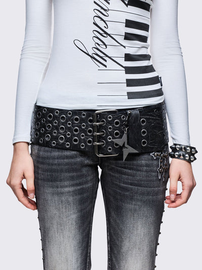Wide black faux leather belt with multiple silver grommets/eyelets across the width, secured by a large triple-pin buckle, with a detachable star charm.