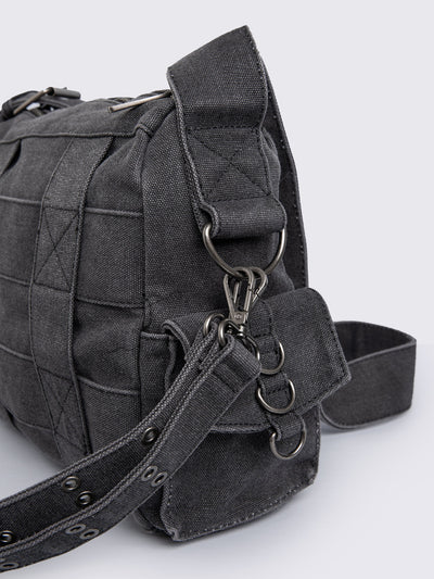 Grey washed denim crossbody bag with all over straps, studs and silver hardware details.