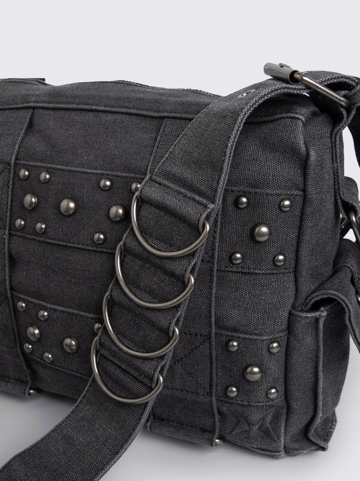 Grey washed denim crossbody bag with all over straps, studs and silver hardware details.