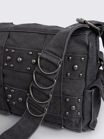 Grey washed denim crossbody bag with all over straps, studs and silver hardware details.