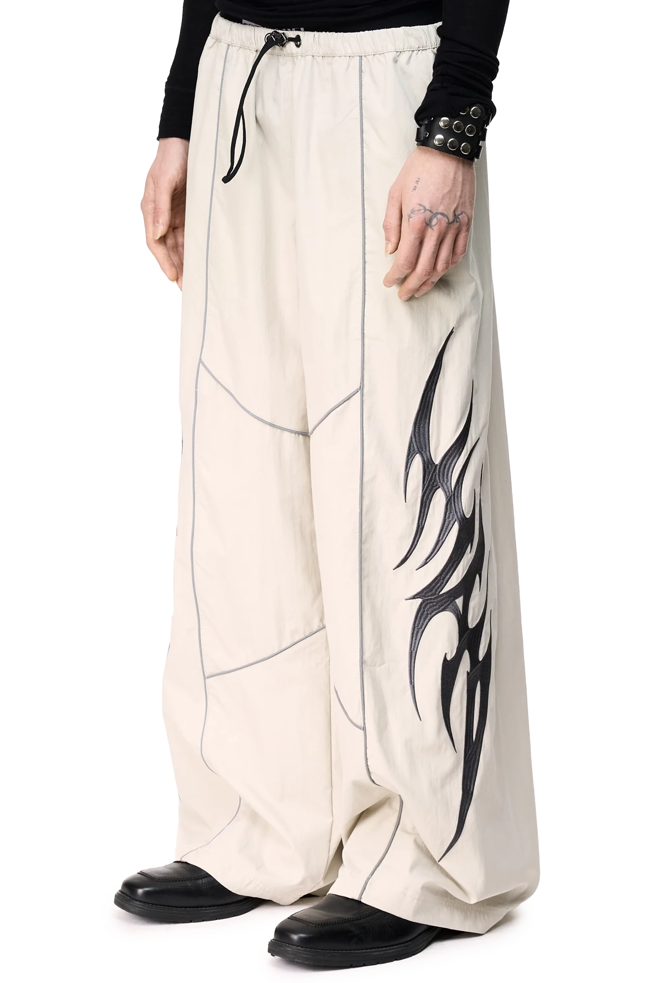 Grey parachute pants with reflective piped seams, sigilism embroidery, side zip pockets and a wide leg fit.