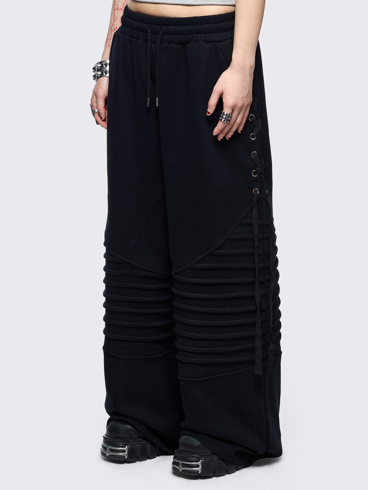 Black wide leg sweatpants featuring moto pintuck panels and lace-up details. 