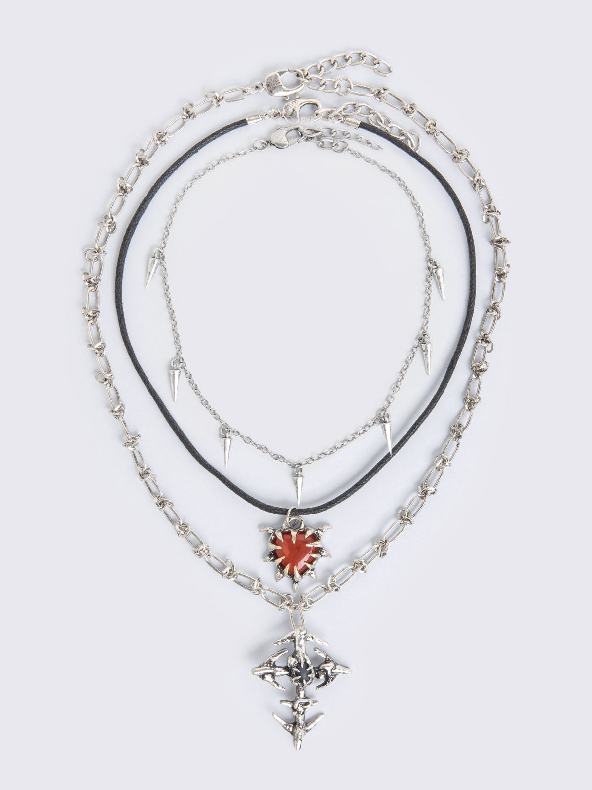 Set of 3 silver necklaces: Cross, spike, and red stone heart pendants in mixed chain styles.