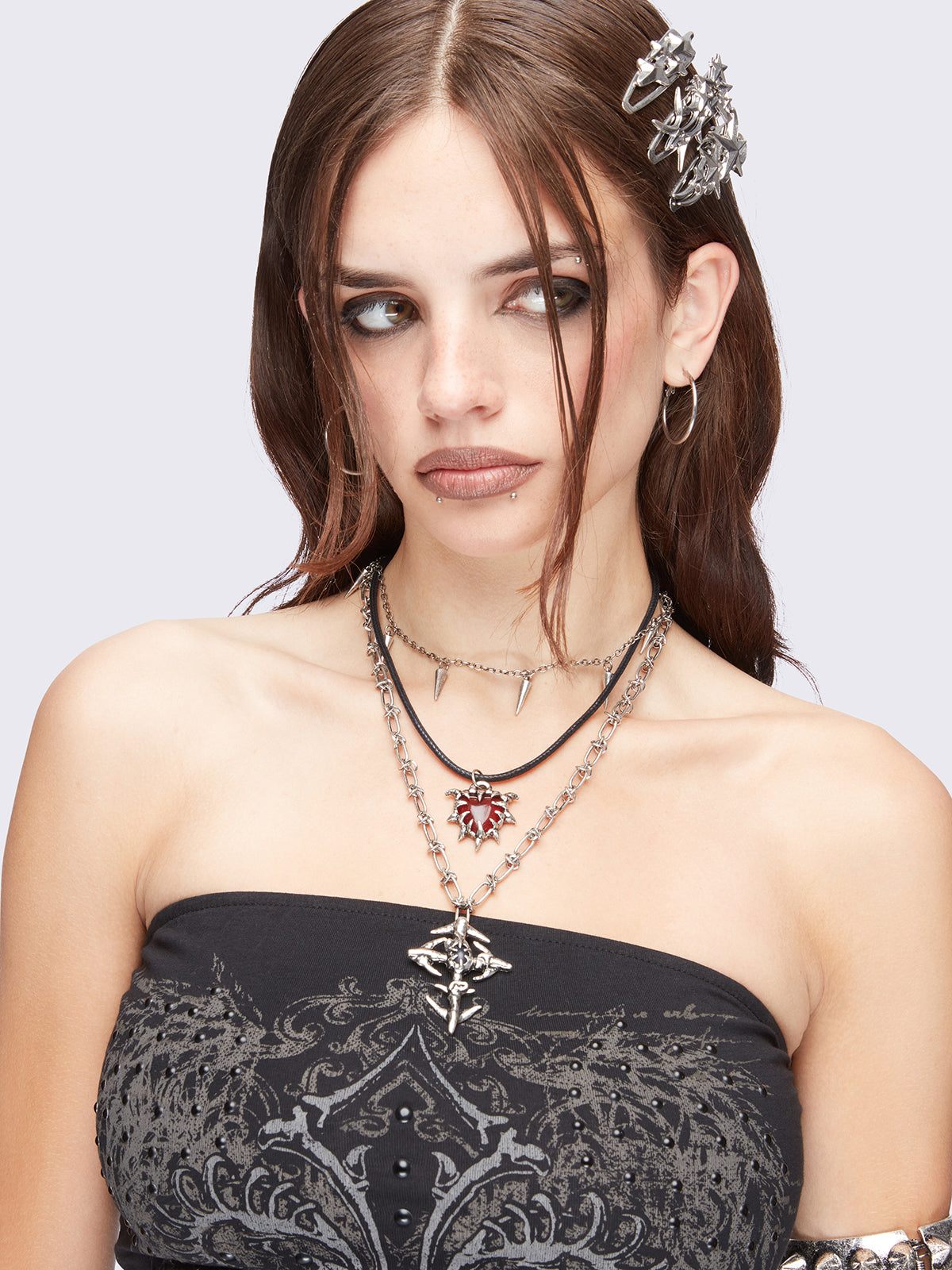 Set of 3 silver necklaces: Cross, spike, and red stone heart pendants in mixed chain styles.