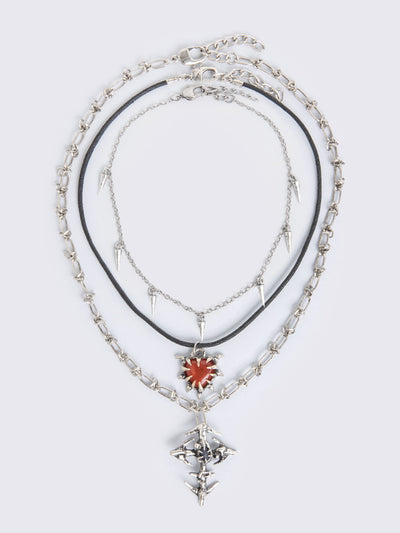 Set of 3 silver necklaces: Cross, spike, and red stone heart pendants in mixed chain styles.